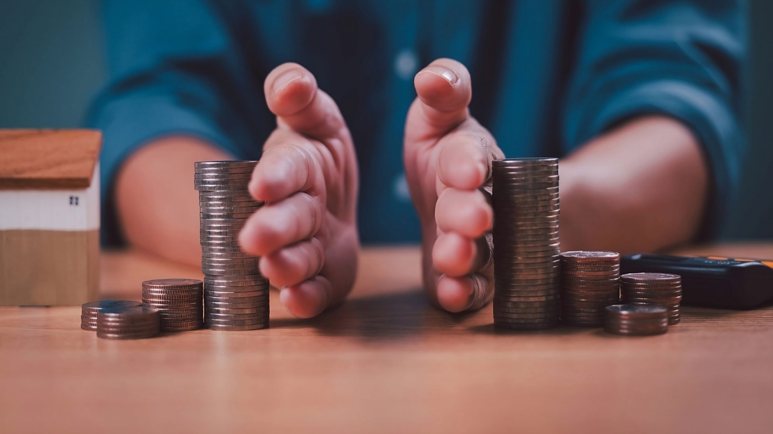 Hands stacking coins next to a model home on a wooden table, representing property protection and affordable estate planning Colorado.