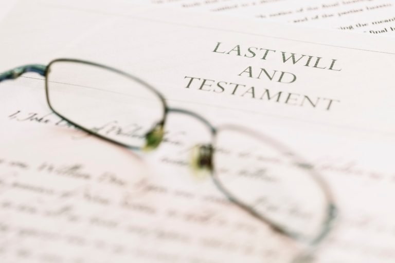 a close up shot of a piece of paper reading Last Will and Testament with a pair of reading glasses sitting with the paper