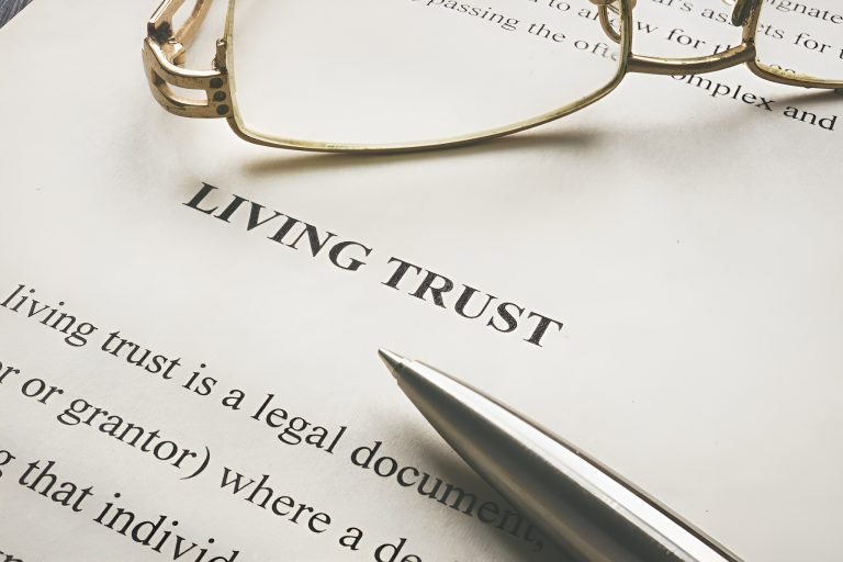 A close-up of a living trust document with a pen and eyeglasses resting on top.