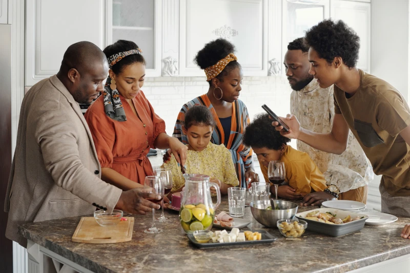 A multi-generational Black family gathered around a kitchen island filled with food and drinks for a celebration, capturing the essence of protecting inheritance second marriage Colorado